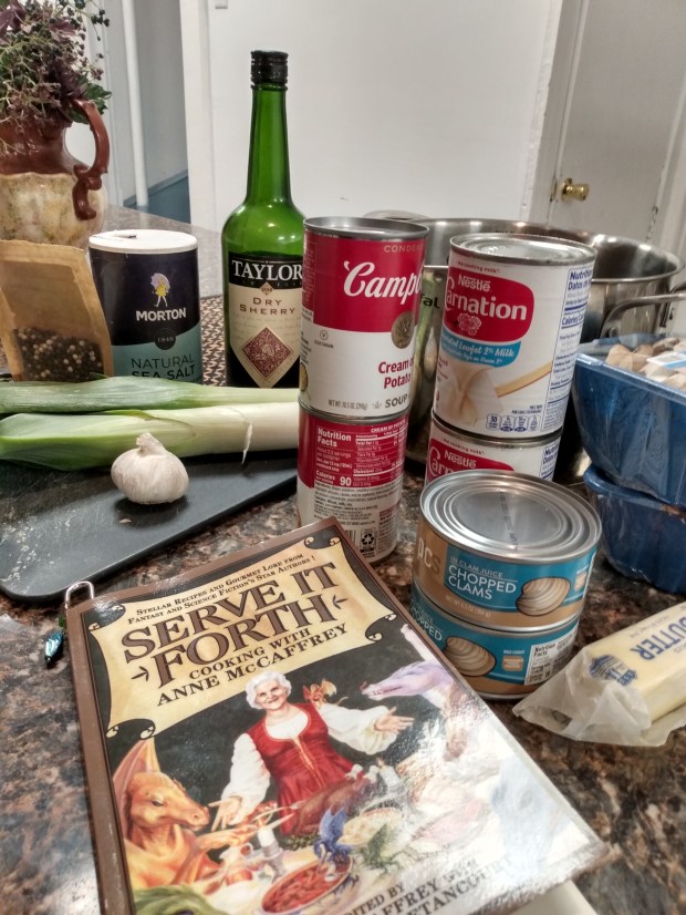 Photo of an array of ingredients for clam chowder clustered on a countertop, including canned clams, canned milk and canned cream of potato soup.